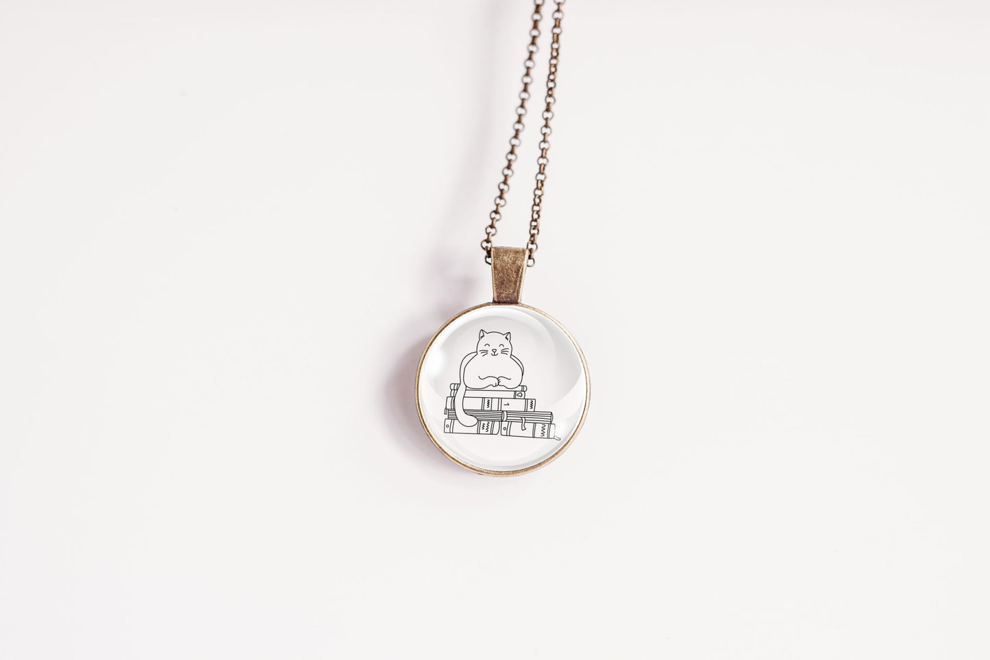 Glass cabochon pendant featuring a black line drawing of a cat sitting on stacked books