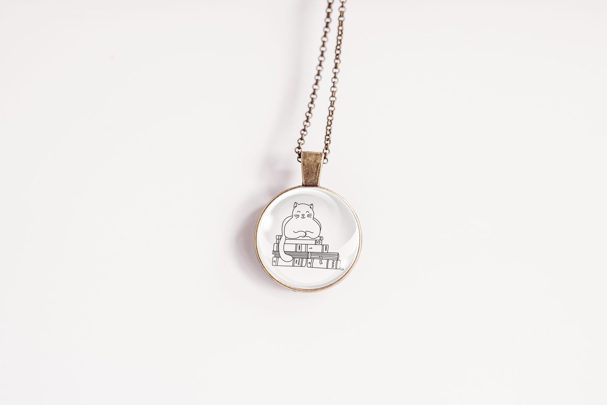 Glass cabochon pendant featuring a black line drawing of a cat sitting on stacked books