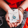 Person holding a dolphin necklace on a 'Whimsy Spirit' card with a red garment in the background.