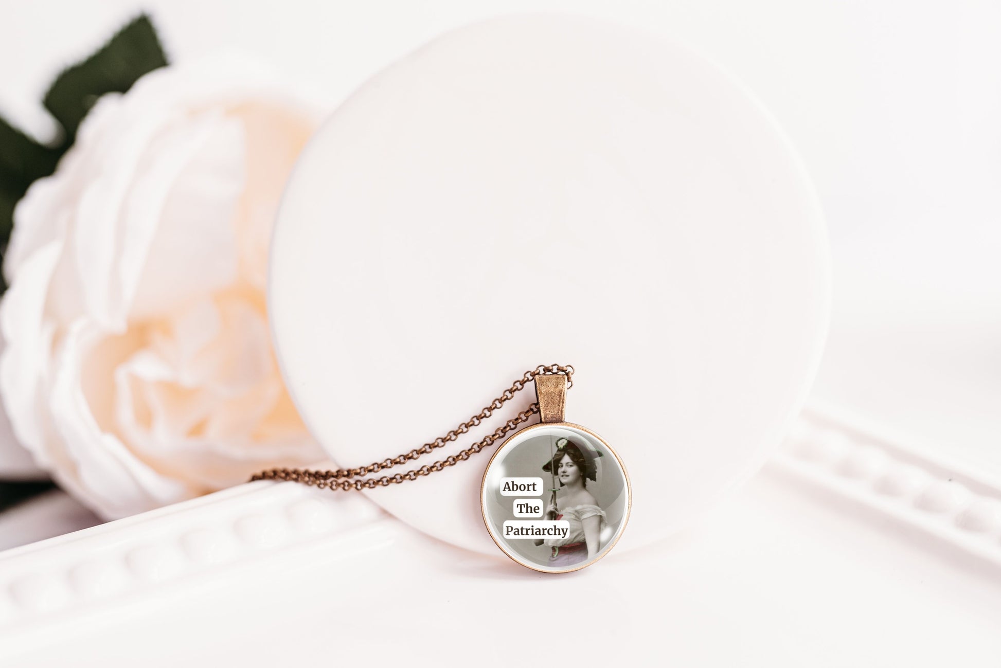 Product photo of a 1-inch glass cabochon pendant necklace featuring “Abort the Patriarchy” with a vintage-style woman holding a sword on a 20-inch chain.