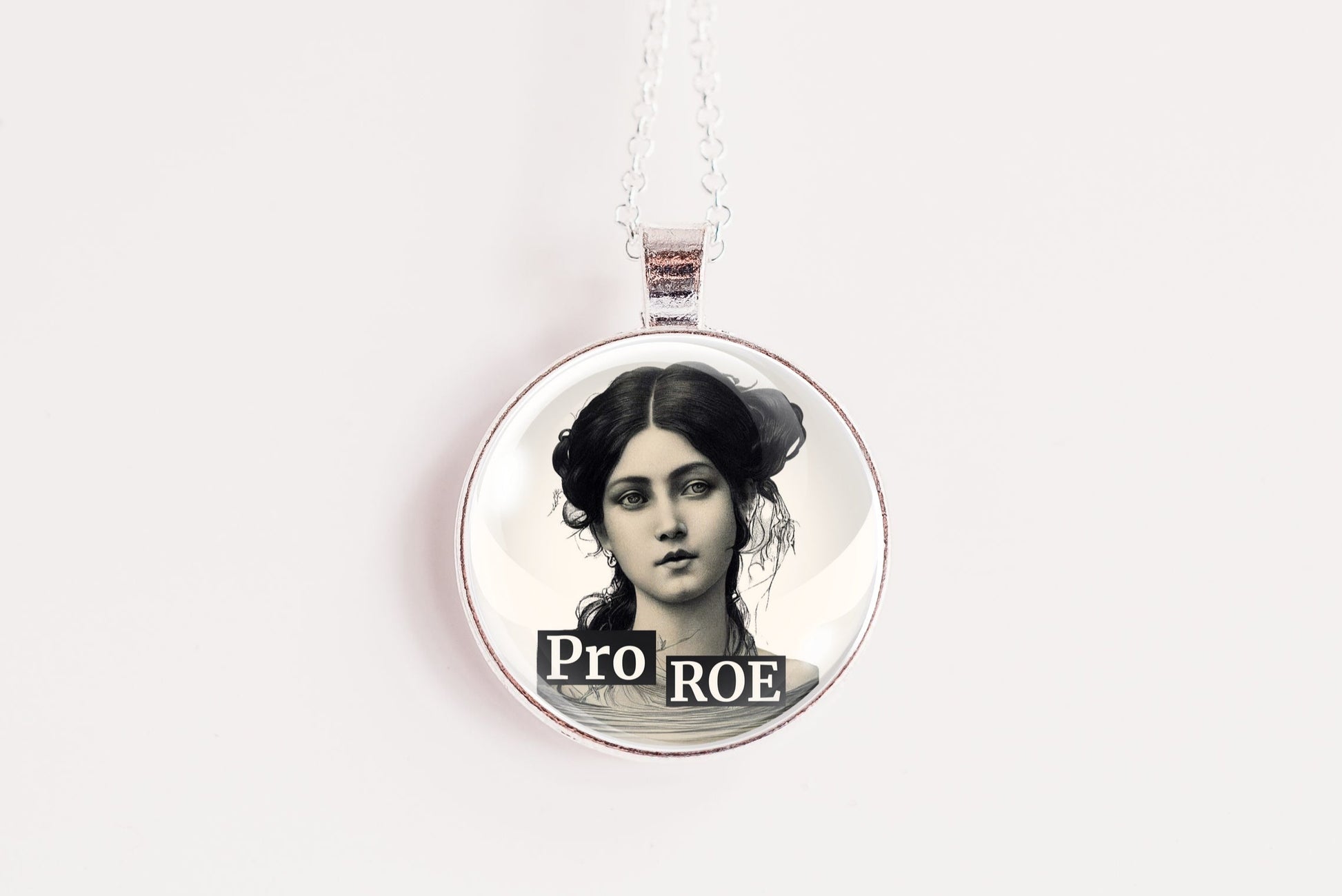 A circular pendant necklace featuring a black and white portrait of a woman with the text 'PRO ROE' printed below, suspended on a thin white cord against a plain white background.