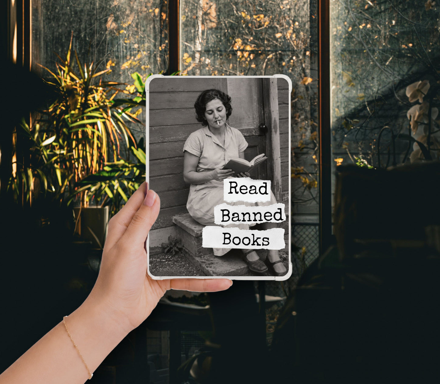 Read Banned Books printable Kindle clear case insert featuring a mid-century woman reading on her porch steps, shown in a clear Kindle case held against a dark botanical background.
