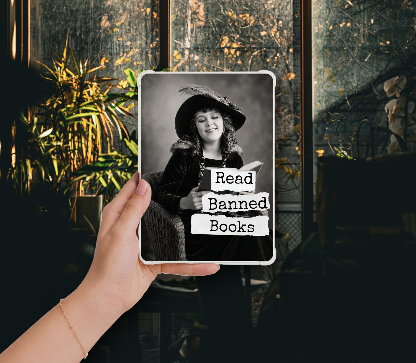 Read Banned Books printable Kindle clear case insert featuring a smiling vintage woman in a wide-brim hat reading a book, shown in a clear Kindle case held against a dark botanical background.