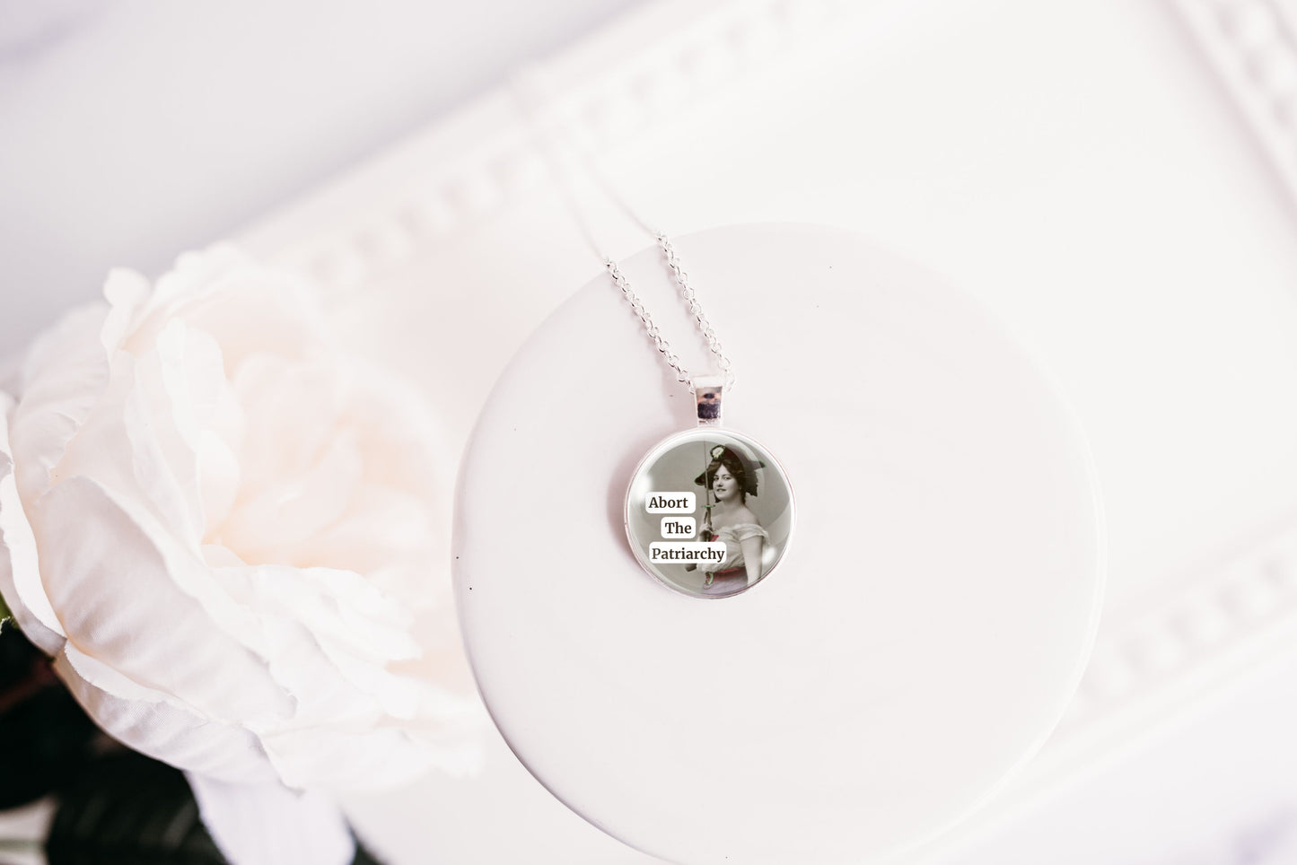 Product photo of a 1-inch glass cabochon pendant necklace featuring “Abort the Patriarchy” with a vintage-style woman holding a sword on a 20-inch chain.