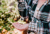 Woman wearing a plaid shirt with a bear necklace and ring, outdoors.