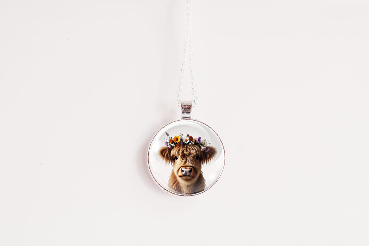 Necklace with a pendant featuring a highland cow with a flower crown on a white surface with a flower in the background