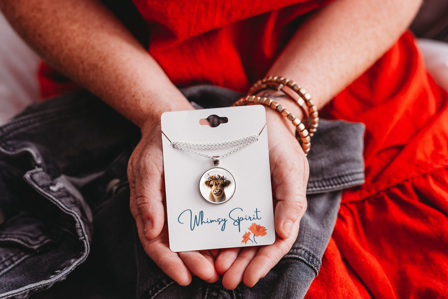 Person holding a highland cow necklace with a pendant on a card labeled 'Whimsy Spirit'
