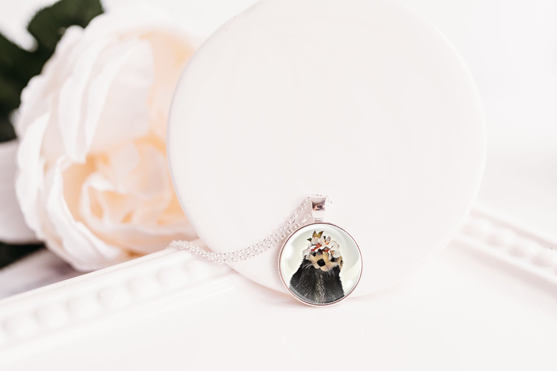 Close-up of an otter necklace with a pendant on a white surface with flowers in the background