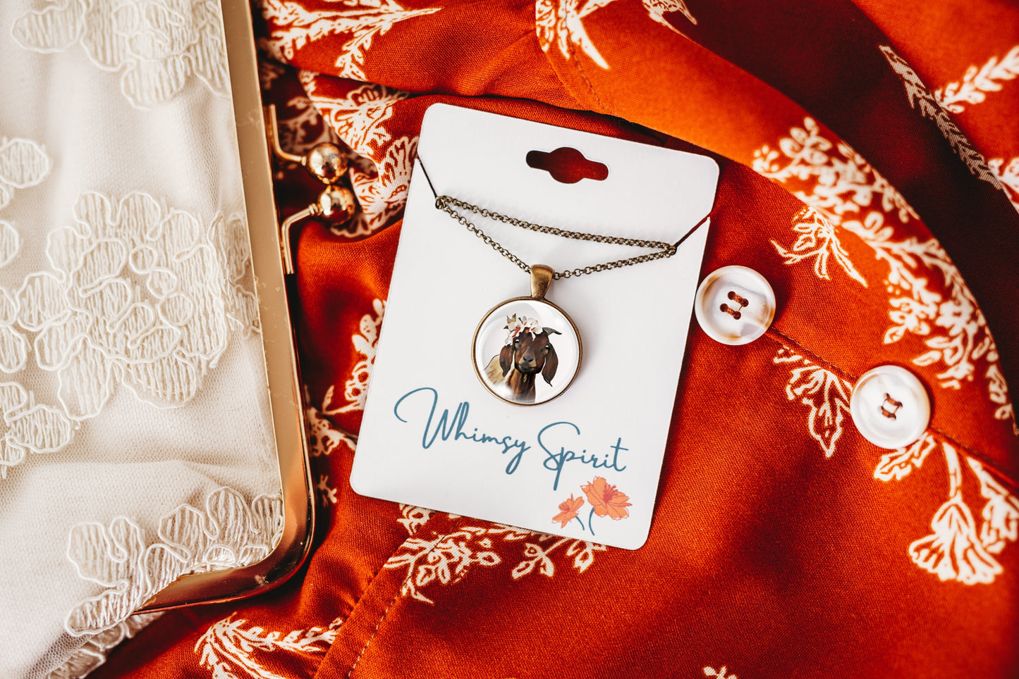 Flower crown goat necklace with pendant on a 'Whimsy Spirit' card on a red fabric background