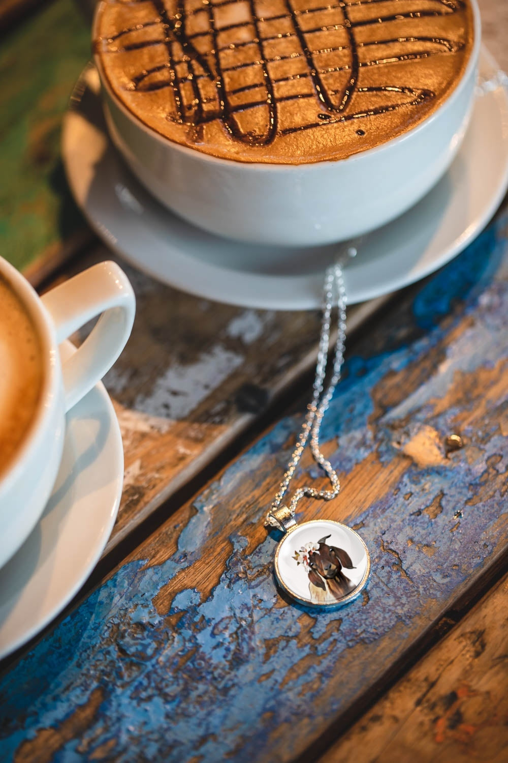 Cup of coffee with a necklace featuring a goat wearing a flower crown on a wooden surface