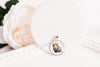 Necklace with a pendant featuring an opossum wearing a flower crown on a white surface with flowers in the background