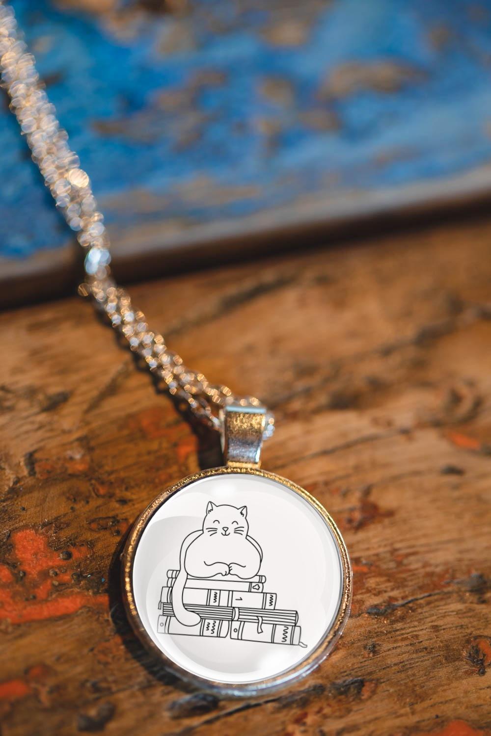 Glass cabochon pendant featuring a black line drawing of a cat sitting on stacked books