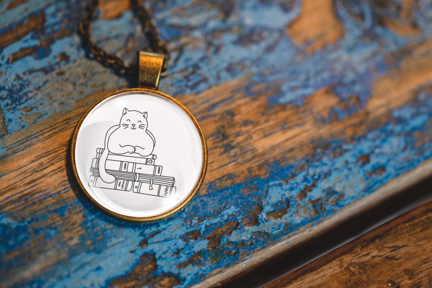 Glass cabochon pendant featuring a black line drawing of a cat sitting on stacked books