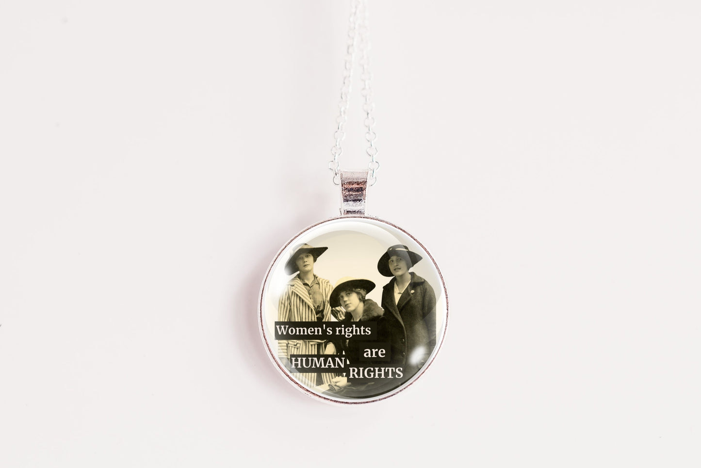 A round pendant necklace featuring a vintage-style illustration of three women with the text 'Women's rights are Human Rights' on a white background.