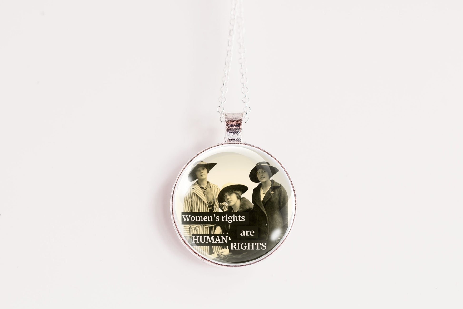 A round pendant necklace featuring a vintage-style illustration of three women with the text 'Women's rights are Human Rights' on a white background.