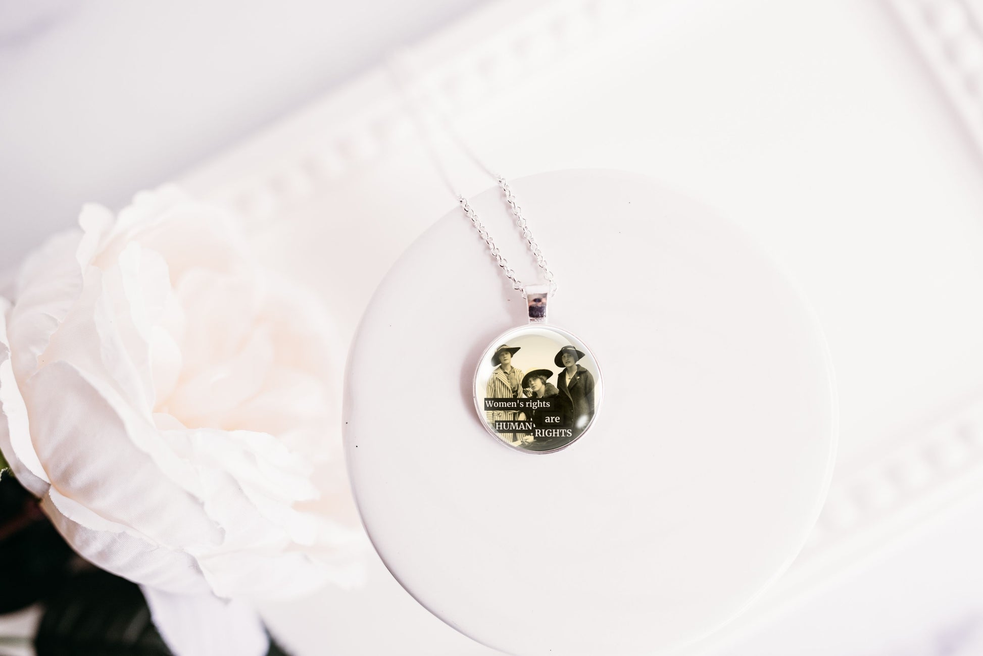 Product photo of a 1-inch glass cabochon pendant necklace featuring “Women’s Rights Are Human Rights” with a group of vintage women in wide-brim hats on a 20-inch chain.