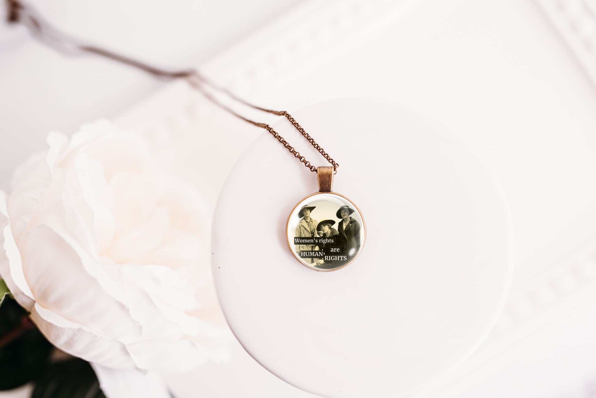 Product photo of a 1-inch glass cabochon pendant necklace featuring “Women’s Rights Are Human Rights” with a group of vintage women in wide-brim hats on a 20-inch chain.
