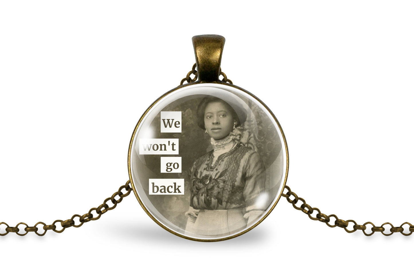 A round pendant necklace with an antique bronze-toned metal frame and chain, featuring a sepia-toned portrait of a woman and the text 'We won't go back' in white lettering on a black background.