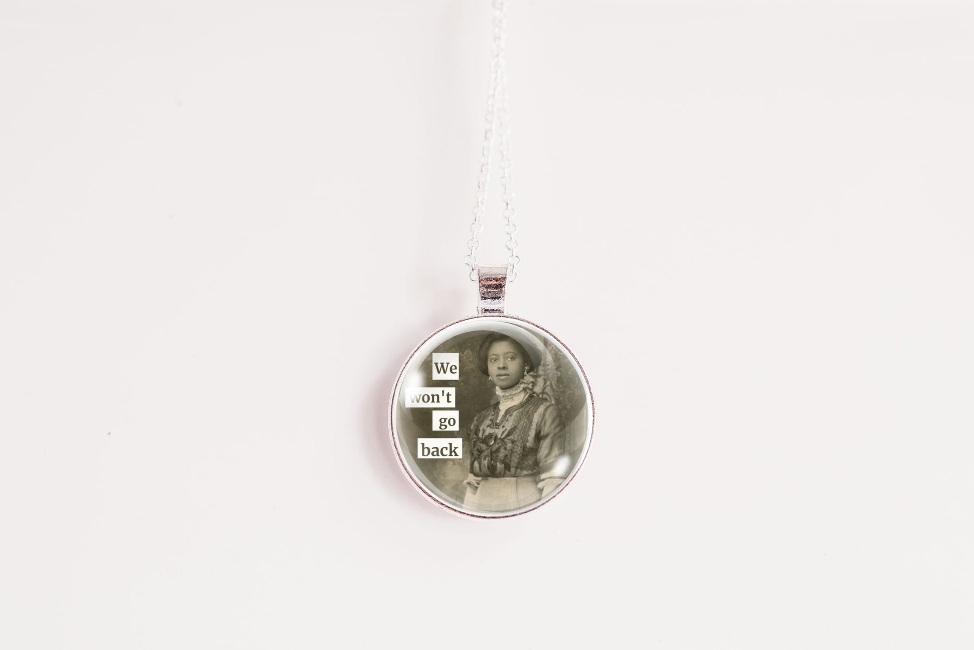 Product photo of a 1-inch glass cabochon pendant necklace featuring “We Won’t Go Back” with a vintage woman standing outdoors on a 20-inch chain.