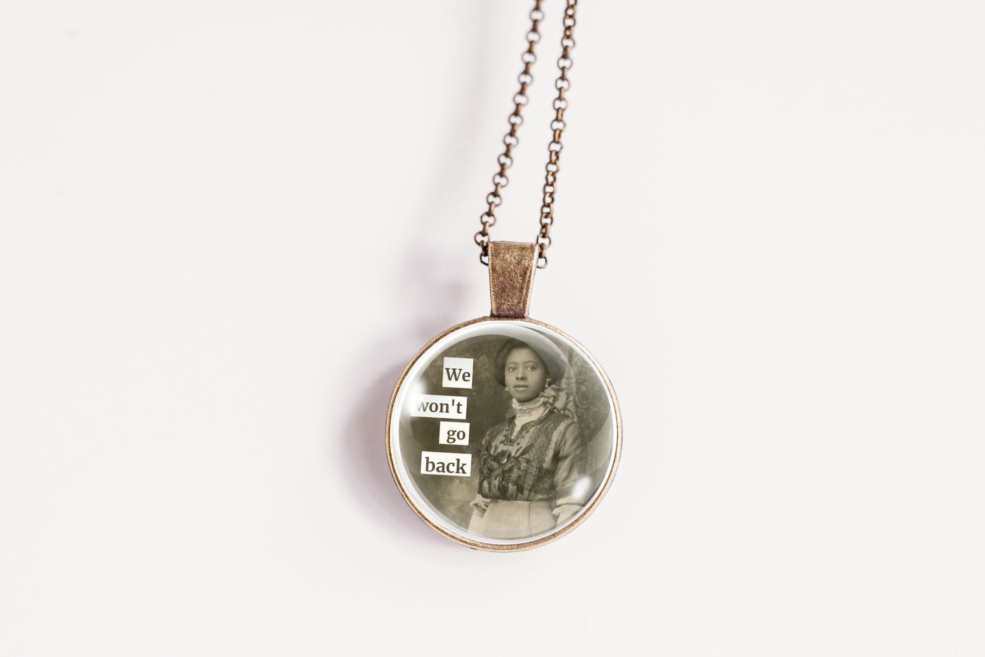 Product photo of a 1-inch glass cabochon pendant necklace featuring “We Won’t Go Back” with a vintage woman standing outdoors on a 20-inch chain.