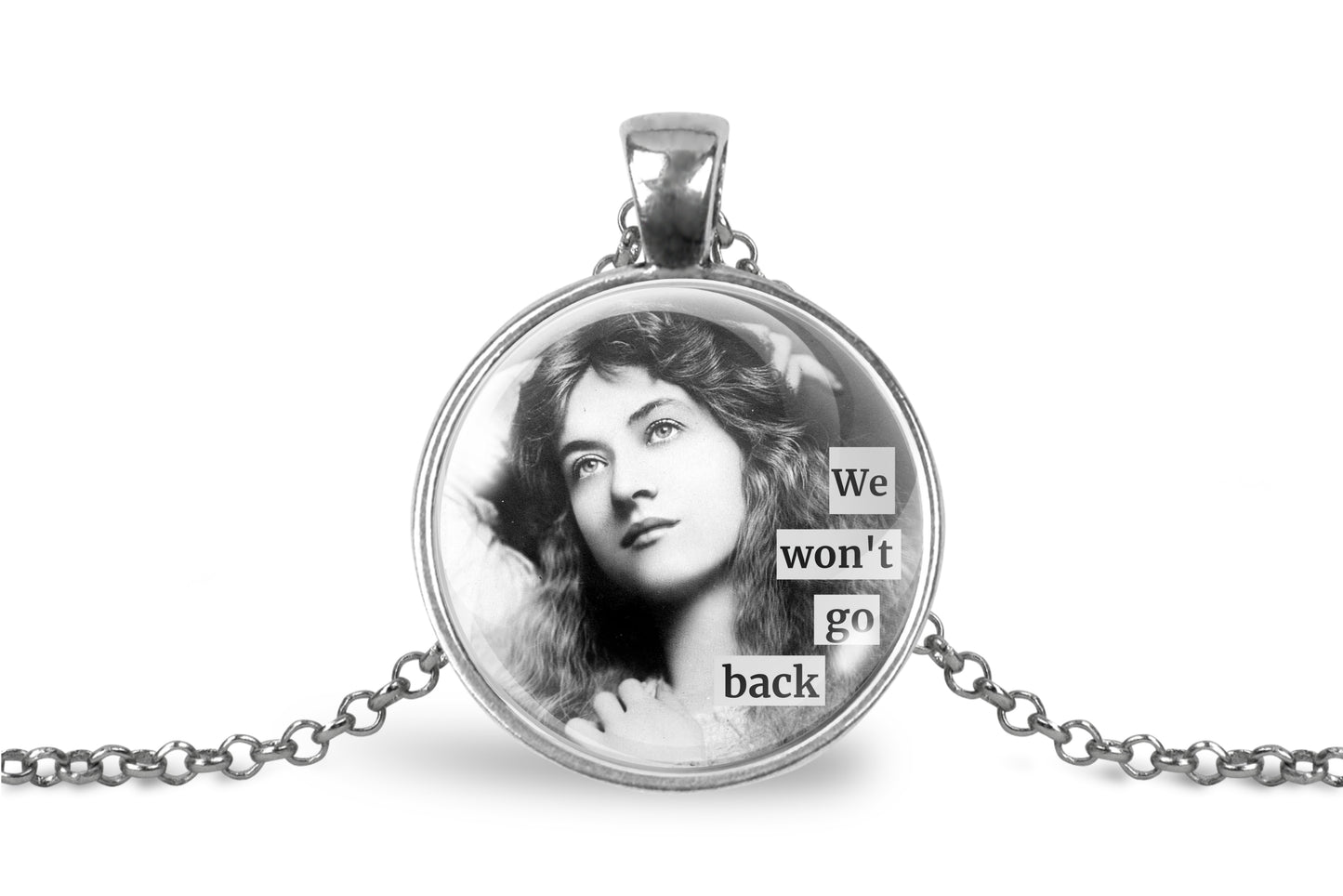 A silver pendant necklace featuring a circular glass cabochon with a black-and-white portrait of a woman and the text 'We won't go back' in stacked letter tiles, shown on a white background with a silver chain extending to both sides.