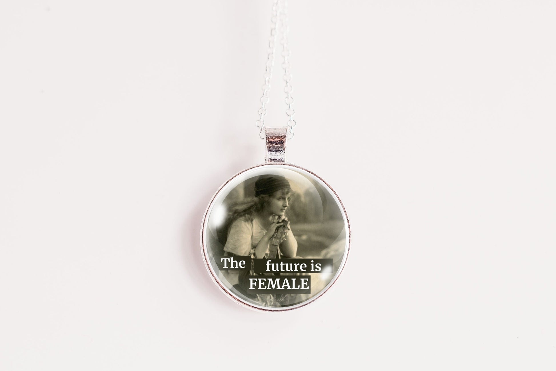 Product photo of a 1-inch glass cabochon pendant necklace featuring “The Future Is Female” with a soft sepia side-profile portrait of a vintage woman on a 20-inch chain.