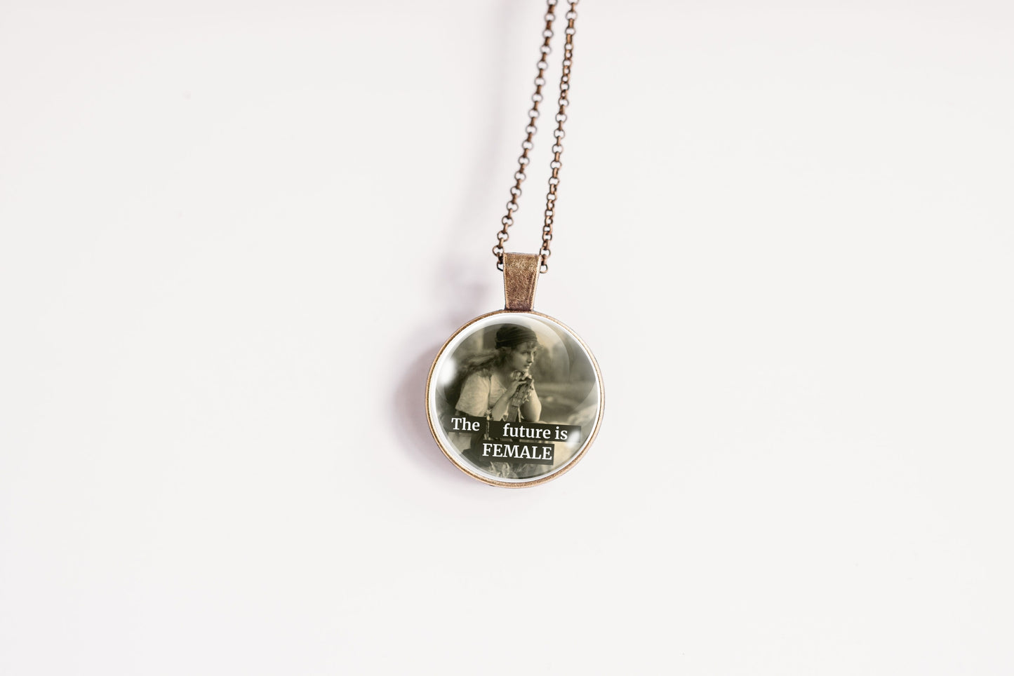 Product photo of a 1-inch glass cabochon pendant necklace featuring “The Future Is Female” with a soft sepia side-profile portrait of a vintage woman on a 20-inch chain.