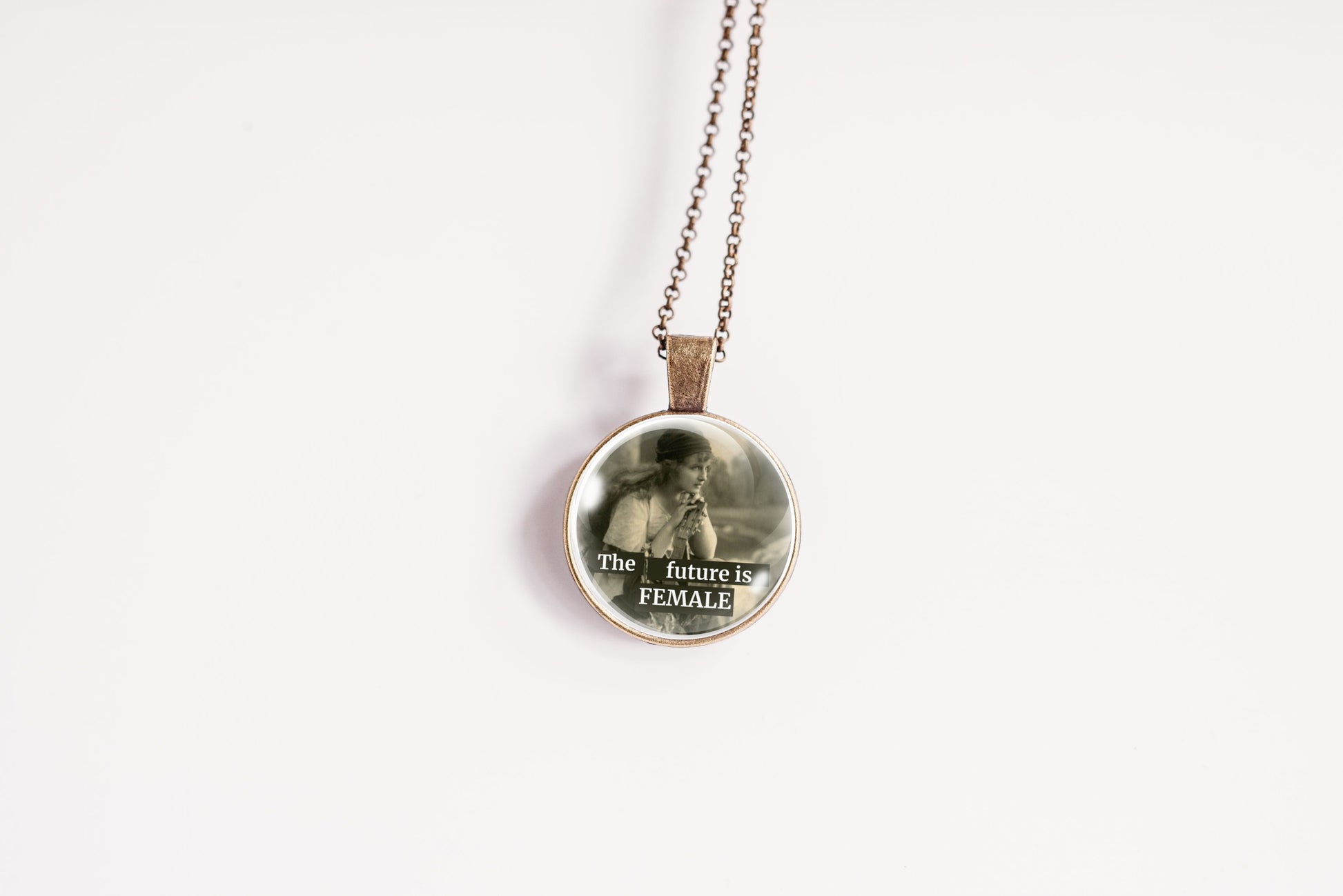 Product photo of a 1-inch glass cabochon pendant necklace featuring “The Future Is Female” with a soft sepia side-profile portrait of a vintage woman on a 20-inch chain.