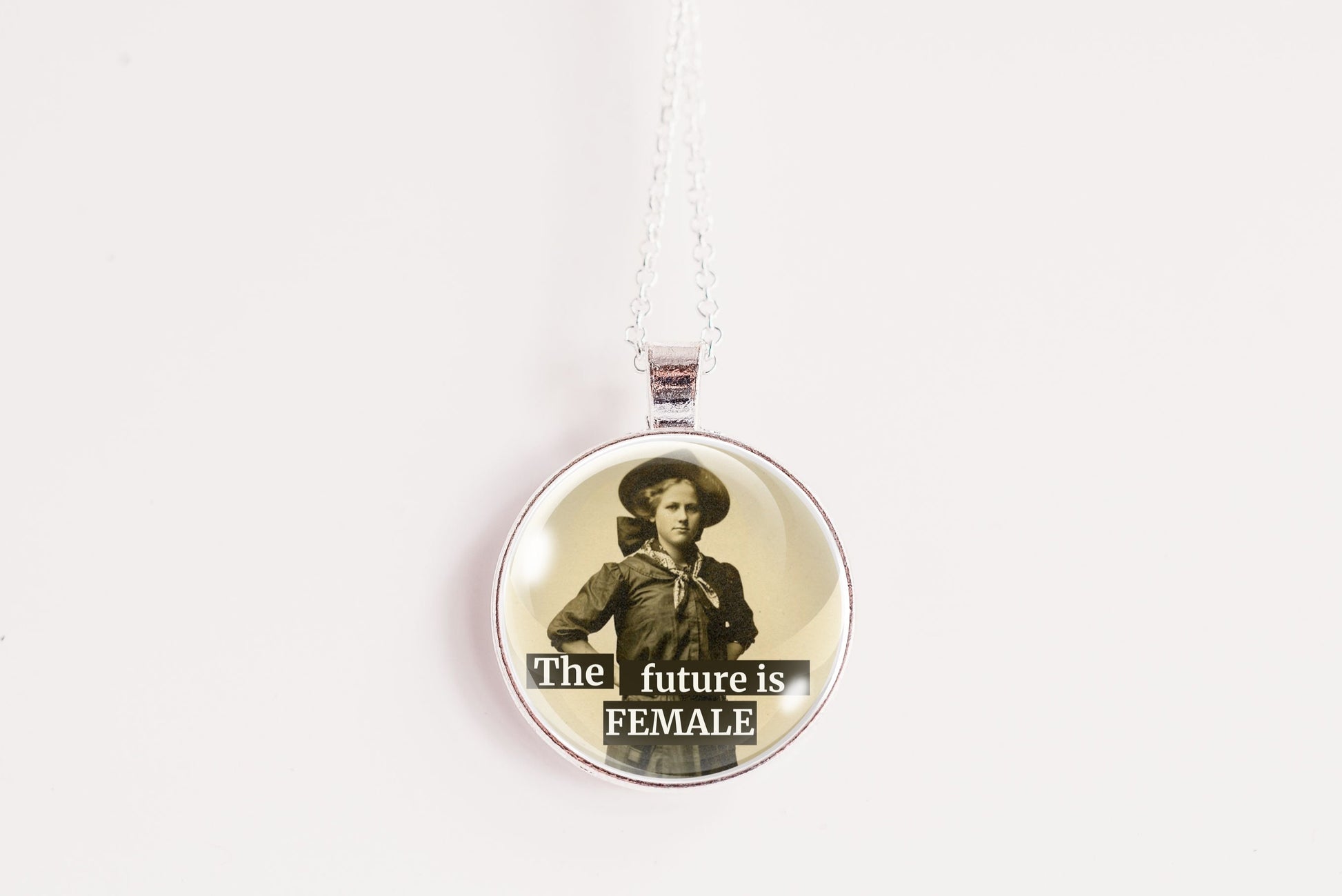 A round pendant necklace featuring a vintage-style portrait of a woman with the text 'The future is FEMALE' printed on the front, suspended from a thin silver chain against a plain white background.