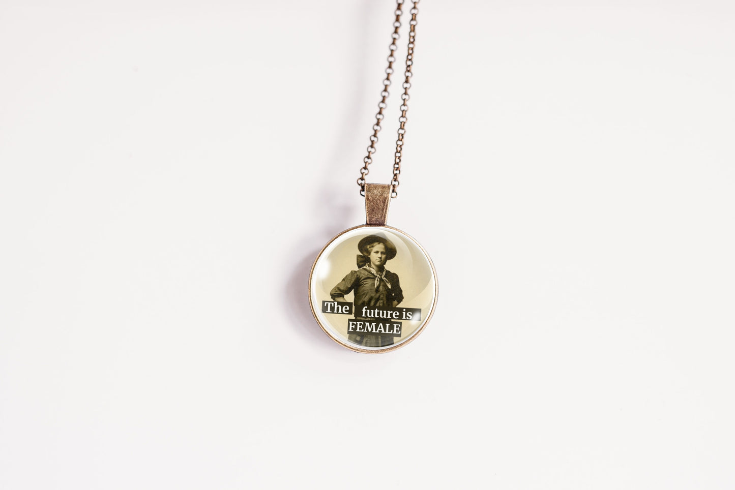 A round pendant necklace on a delicate chain, featuring a vintage-style sepia portrait of a woman with the text 'the future is FEMALE' printed on the front, set against a plain white background.