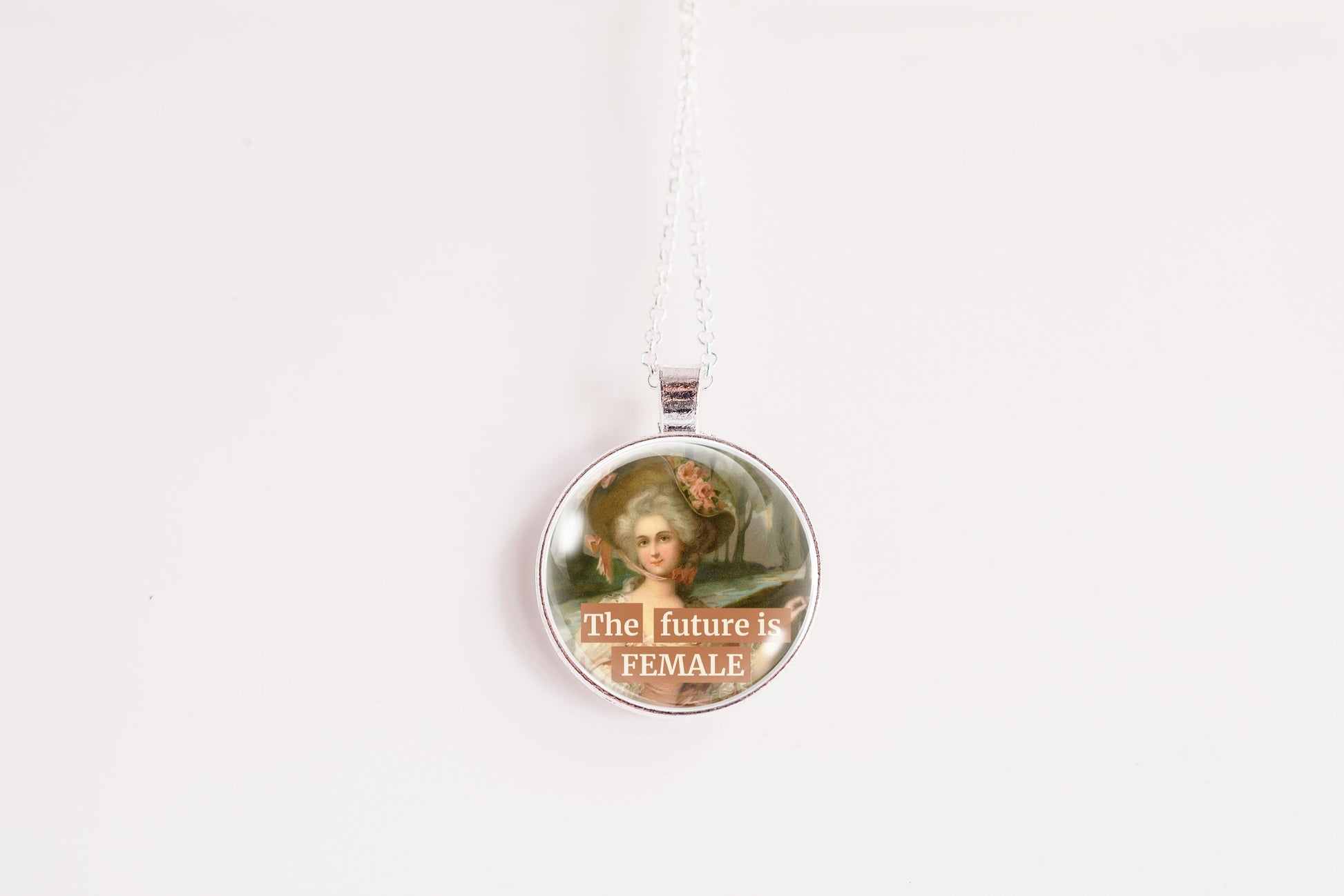 A round pendant necklace featuring a vintage portrait of a woman with the text 'The future is FEMALE' printed on the front, suspended from a silver-toned chain against a plain white background.