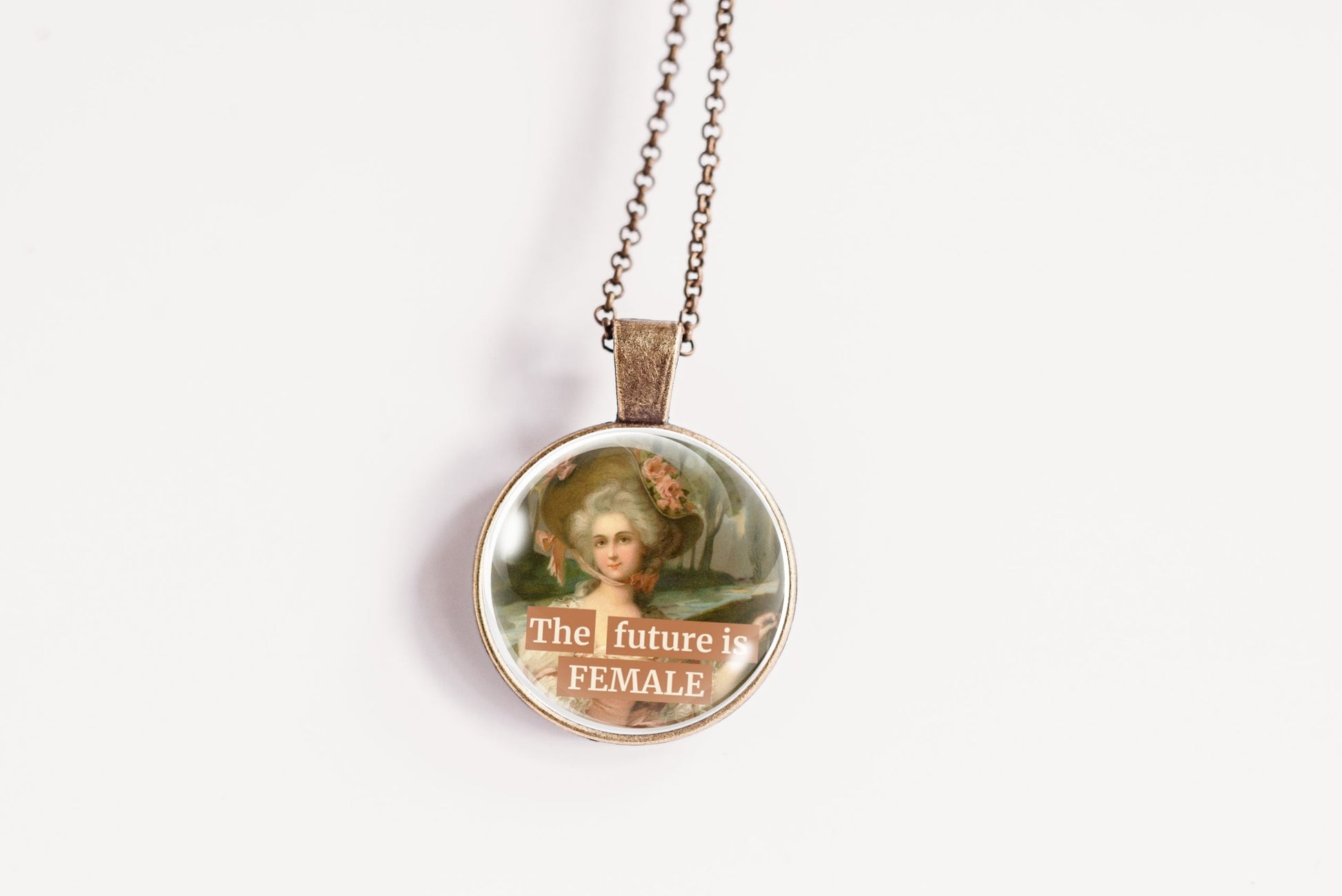 A round pendant necklace on a delicate chain, featuring a vintage-style portrait of a woman with the text 'The future is FEMALE' printed on the bottom of the pendant.