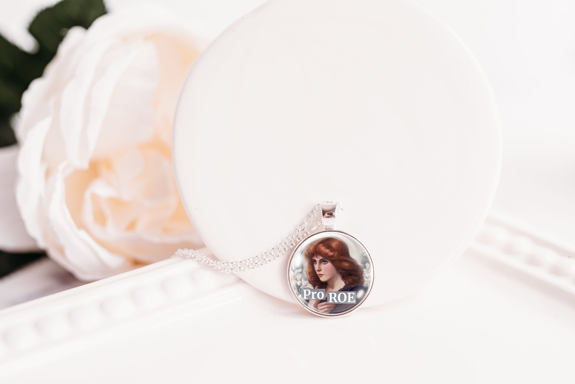 A silver-toned necklace with a round pendant featuring a printed photo of a woman and the text 'Pro ROE'