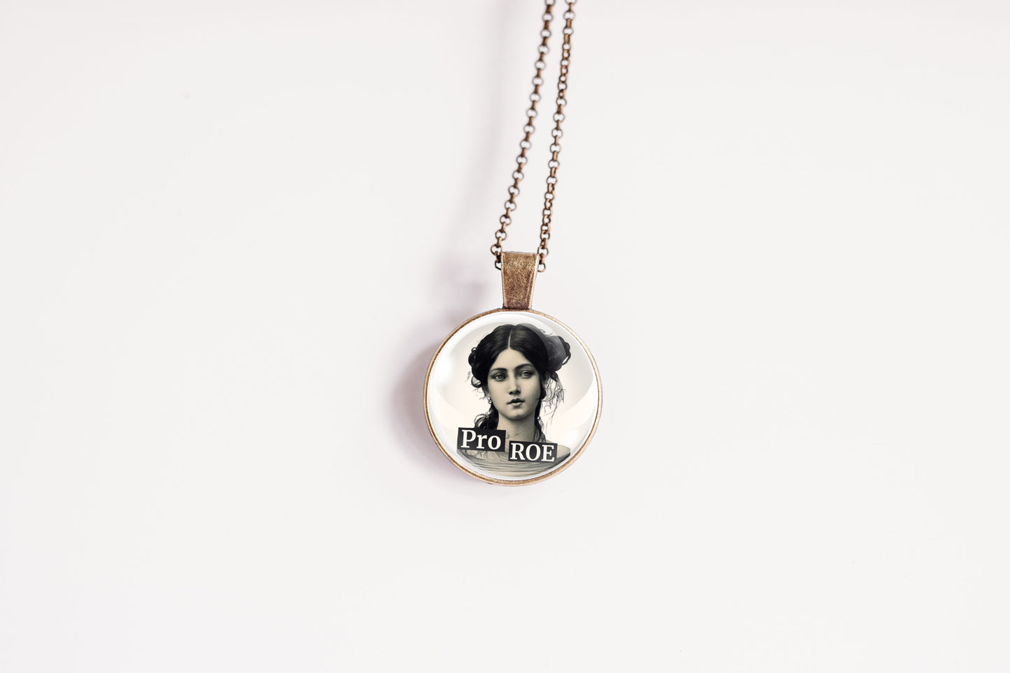 A round pendant necklace featuring a black-and-white portrait of a woman with the text 'PRO ROE' printed below, hanging from a thin chain against a plain white background.