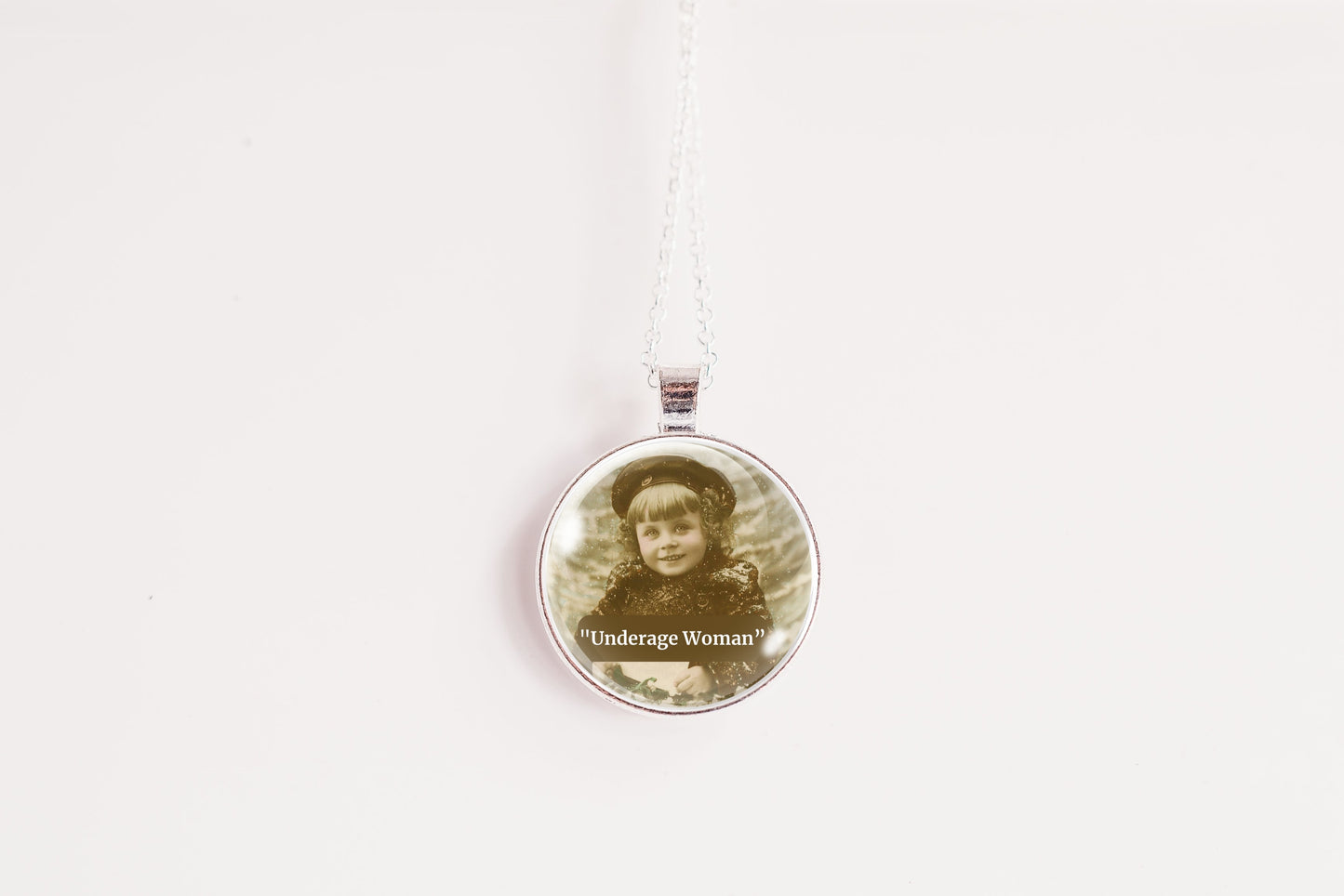 A round pendant necklace featuring a vintage sepia-toned portrait of a woman in a hat, with the text "Underage Woman" printed below the photo. The pendant is suspended from a silver-toned chain against a plain white background.