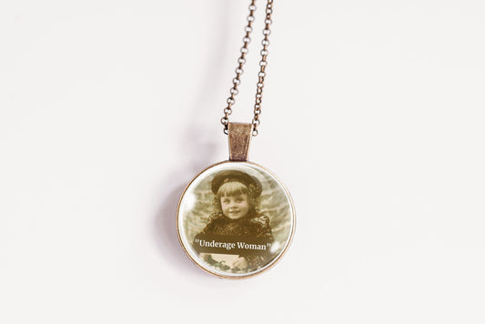 A round pendant necklace on a delicate chain, featuring a vintage-style sepia portrait of a young girl with the text 'Underdog Woman' printed below, set against a plain white background.