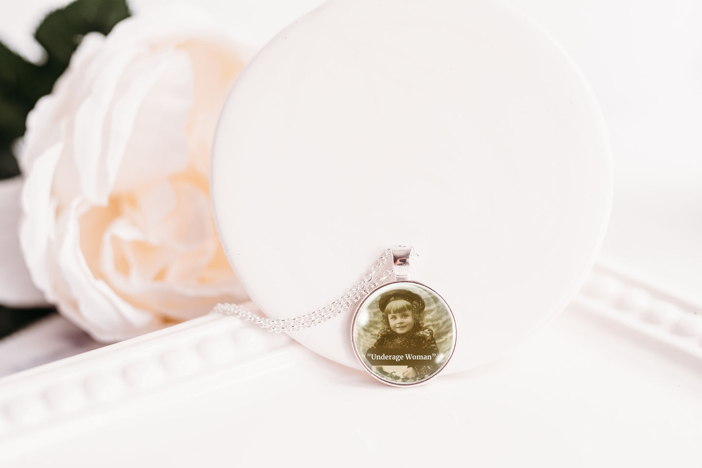 Product photo of a 1-inch glass cabochon pendant necklace featuring “Underage Woman” with a sepia portrait of a young vintage girl on a 20-inch chain.