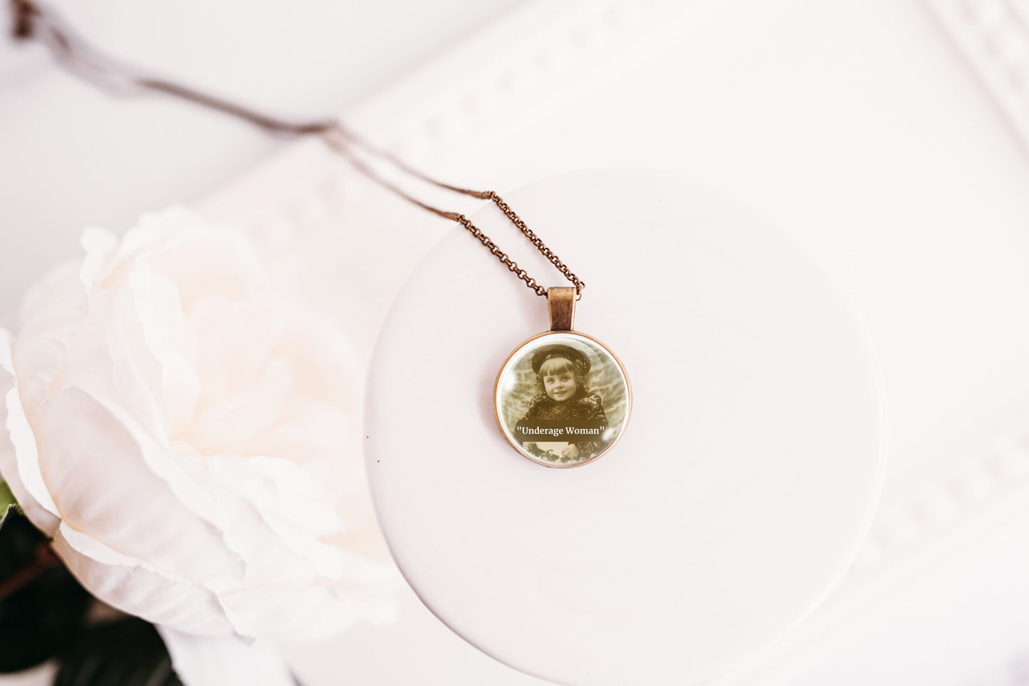 Product photo of a 1-inch glass cabochon pendant necklace featuring “Underage Woman” with a sepia portrait of a young vintage girl on a 20-inch chain.