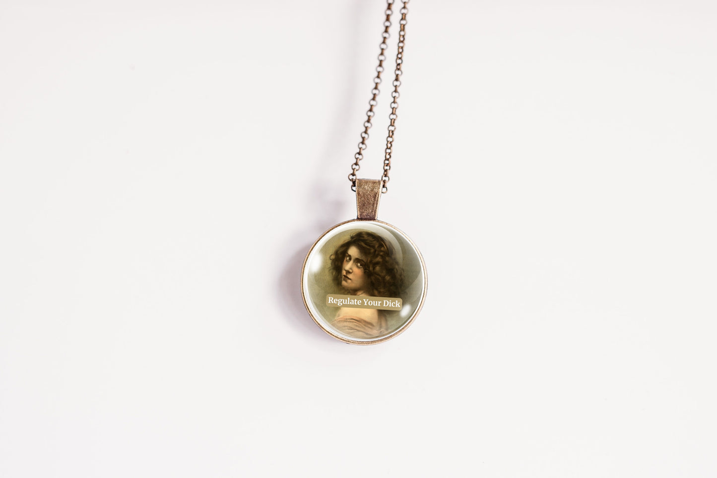 Product photo of a 1-inch glass cabochon pendant necklace featuring “Regulate Your Dick” with a sepia portrait of a curly-haired vintage woman on a 20-inch chain.