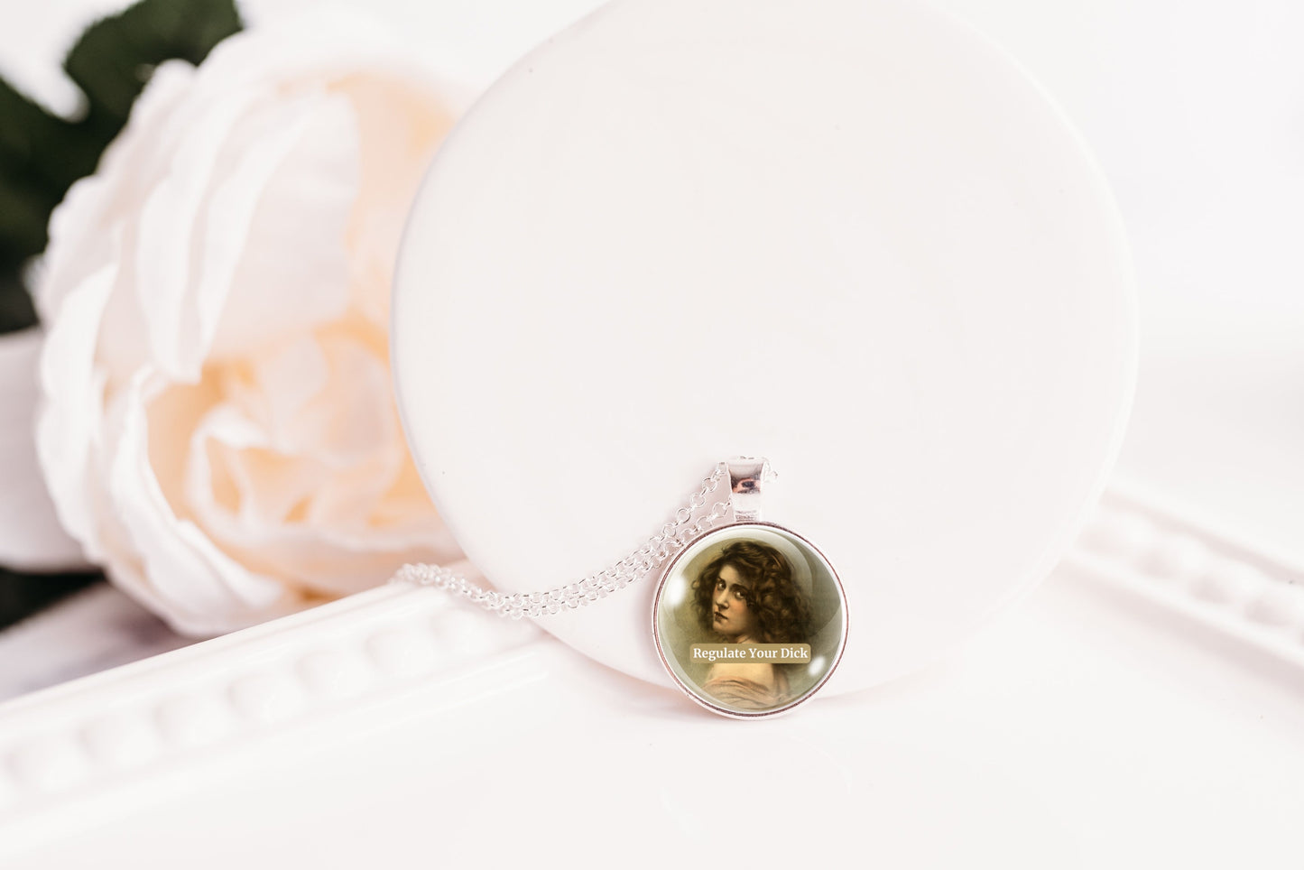 Product photo of a 1-inch glass cabochon pendant necklace featuring “Regulate Your Dick” with a sepia portrait of a curly-haired vintage woman on a 20-inch chain.