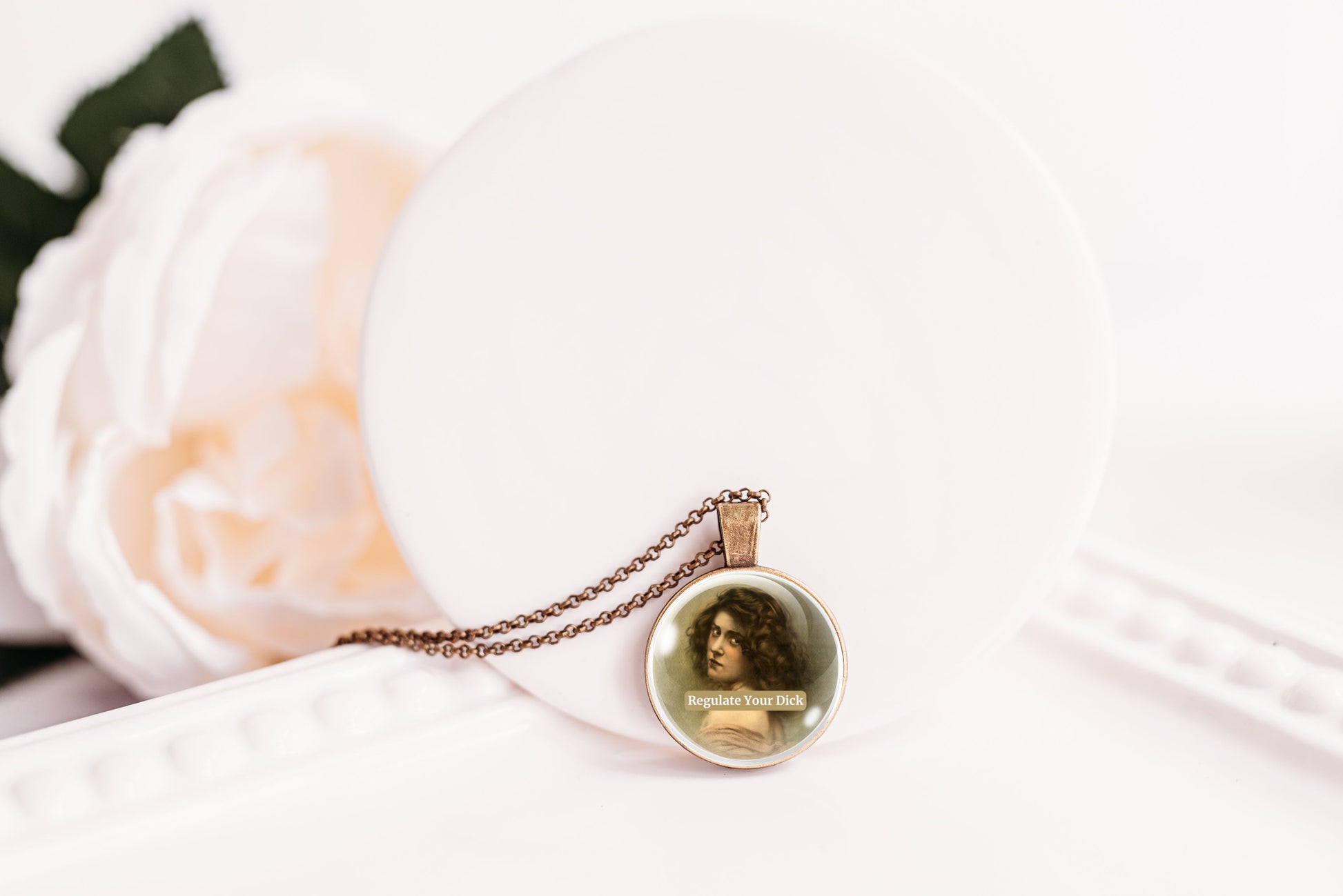 Product photo of a 1-inch glass cabochon pendant necklace featuring “Regulate Your Dick” with a sepia portrait of a curly-haired vintage woman on a 20-inch chain.
