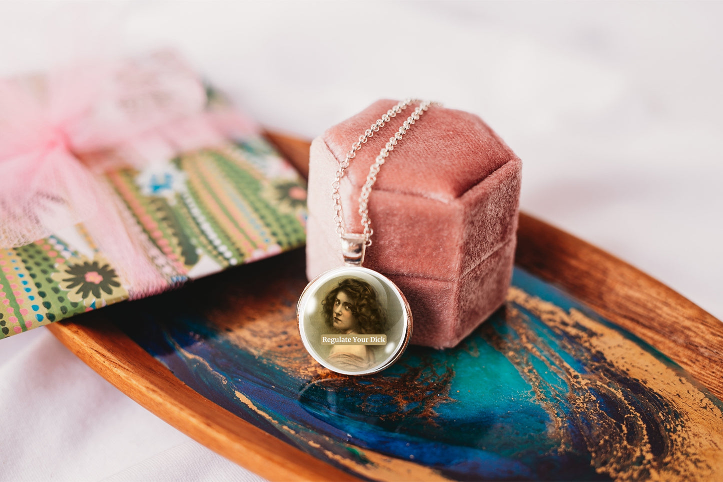 Product photo of a 1-inch glass cabochon pendant necklace featuring “Regulate Your Dick” with a sepia portrait of a curly-haired vintage woman on a 20-inch chain.