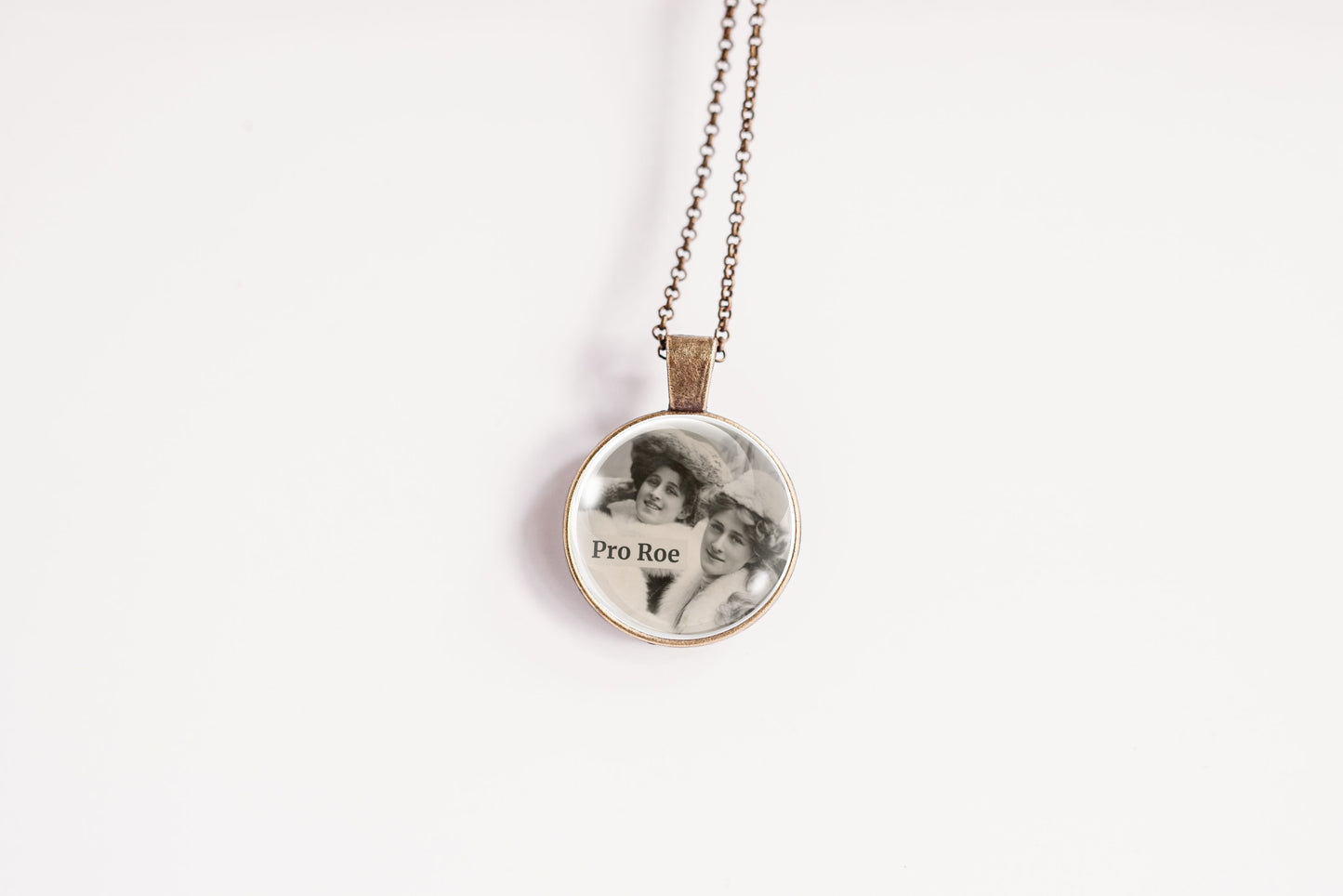 A round pendant necklace on a delicate chain, featuring a black-and-white portrait photo with the text 'Pro Roe' printed on it, set against a plain white background.