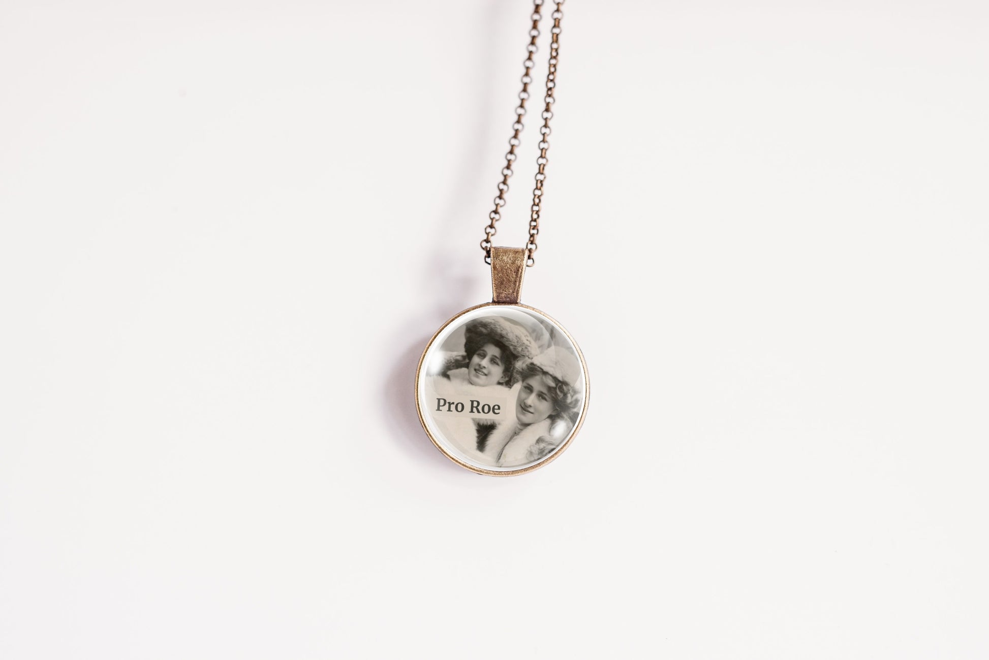 A round pendant necklace on a delicate chain, featuring a black-and-white portrait photo with the text 'Pro Roe' printed on it, set against a plain white background.