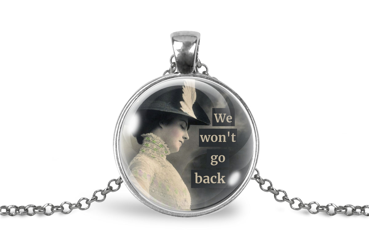 A silver pendant necklace featuring a round glass dome with a vintage-style photo of a woman in profile and the text 'We won't go back' in white lettering, shown on a white background with a silver chain.