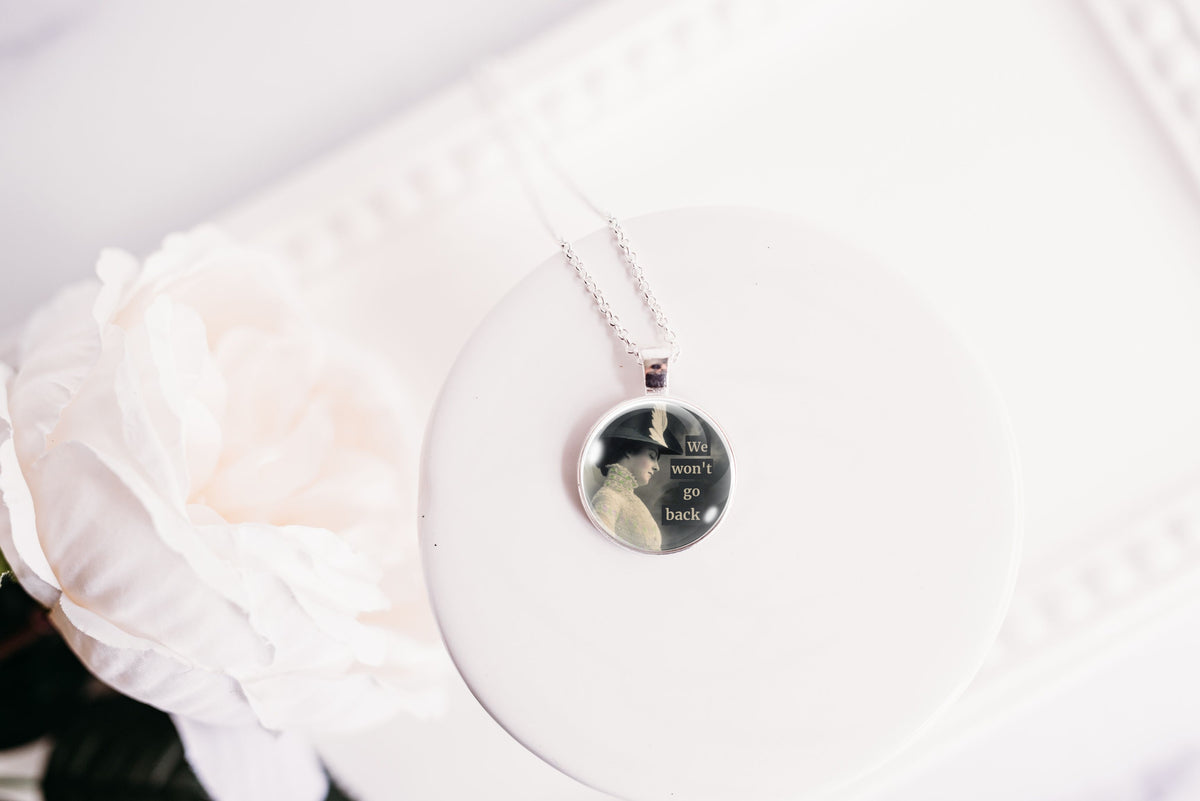 Product photo of a 1-inch glass cabochon pendant necklace featuring “We Won’t Go Back” with a side-profile vintage woman in a dark hat on a 20-inch chain.