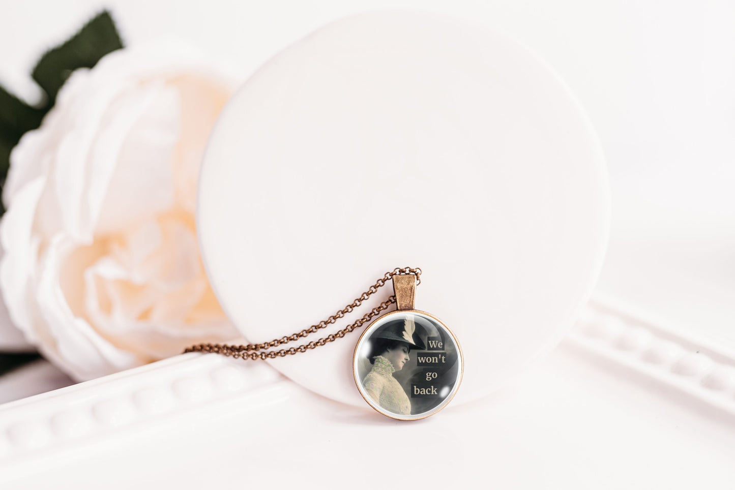 Product photo of a 1-inch glass cabochon pendant necklace featuring “We Won’t Go Back” with a side-profile vintage woman in a dark hat on a 20-inch chain.