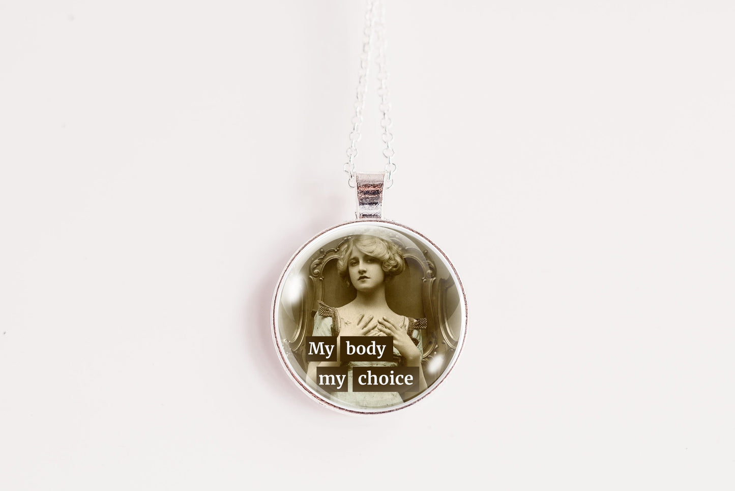 A silver pendant necklace featuring a circular glass dome with a sepia-toned vintage illustration of a woman and the text 'My body my choice' in white, suspended against a plain white background.