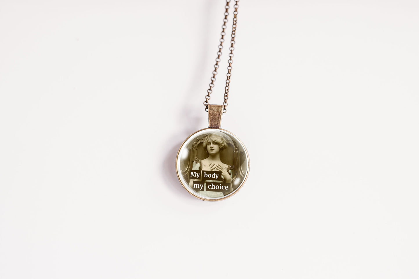 A round pendant necklace on a delicate chain, featuring a vintage-style sepia portrait of a woman with the words 'My body my choice' in a typographic collage design, set against a plain white background.