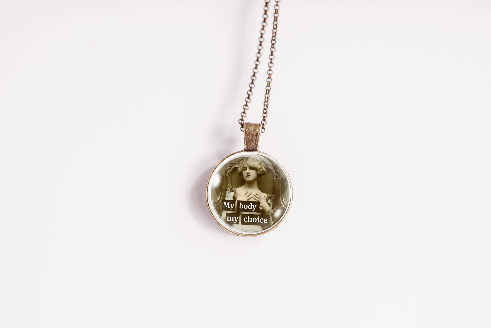 A round pendant necklace on a delicate chain, featuring a vintage-style sepia portrait of a woman with the words 'My body my choice' in a typographic collage design, set against a plain white background.